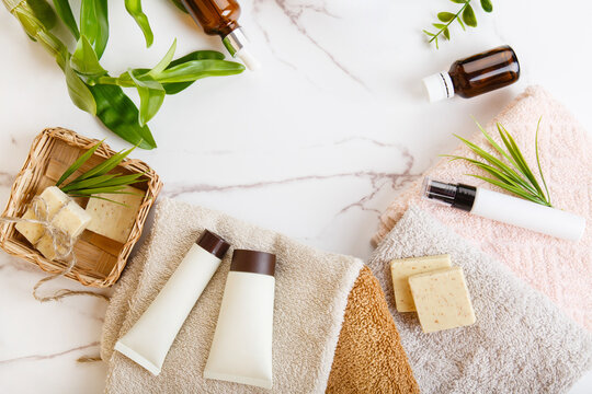 Spa and bath cosmetics, basket with serum and face gel, towel rolls, natural soap on white marble background. Natural face care products in bathroom. Eco-friendly cosmetics with plants. Natural beauty