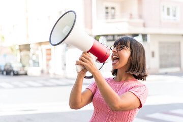 Young brunette woman in the city shouting through a megaphone to announce something in lateral...