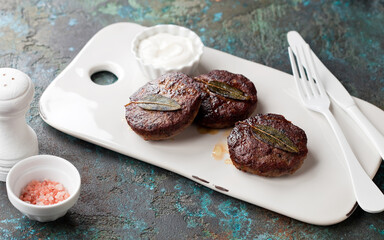 Roasted homemade lamb cutlets with sage on a white serving board, selective focus
