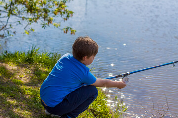 The boy is sitting on the shore of the lake with a fishing rod and fishing. The little fisherman. A child is fishing in the river.