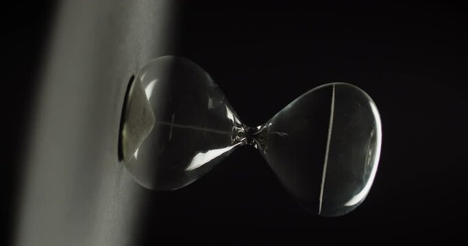An hourglass slowly rotating on black background. Abstract running time concept.