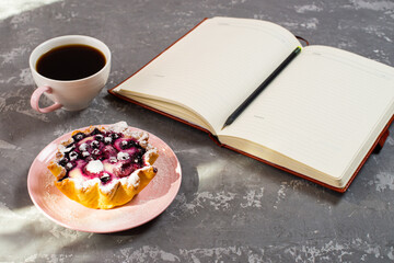 Notepad, a cup of coffee and a cake basket with berries and cottage cheese on a concrete table. Flatley coffee break layout.