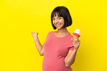 Pregnant woman holding a cornet ice cream isolated on yellow background extending hands to the side for inviting to come