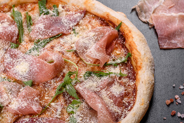 Fresh delicious Italian pizza with a prosciutto on a dark concrete background