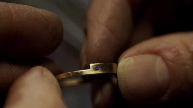 Closeup of a golden engagement ring with a diamond freshly made being inspected in jewellers hands.