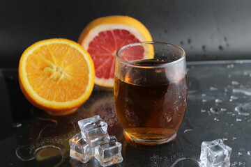 Apple citrus dark juice in a glass next to lies citrus orange grapefruit ice on a black background. Refreshing drinks, summer, soft drinks