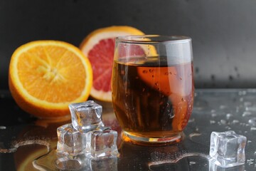 Apple citrus dark juice in a glass next to lies citrus orange grapefruit ice on a black background. Refreshing drinks, summer, soft drinks