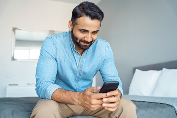 Indian man checking email message chatting social network using phone sit on bed