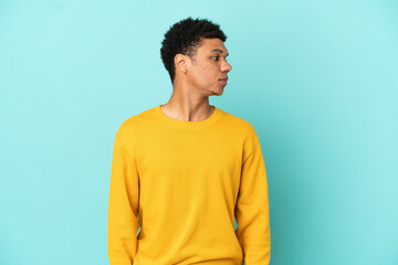 Young African American man isolated on blue background looking to the side