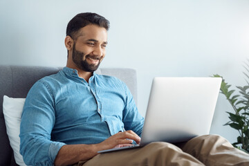Happy smiling indian businessman working from home using laptop computer