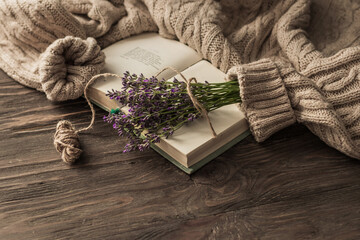 Cozy morning. Lavender bouquet on an open book and a warm sweater on a wooden table. Still life concept.
