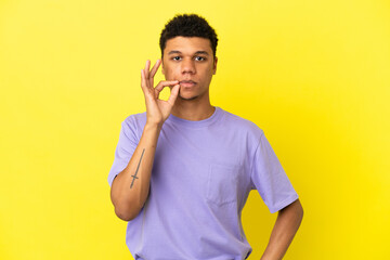 Young African American man isolated on yellow background showing a sign of silence gesture