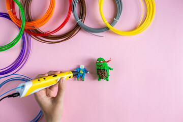 Children's hands create figures with a 3D pen on the pink background, top view