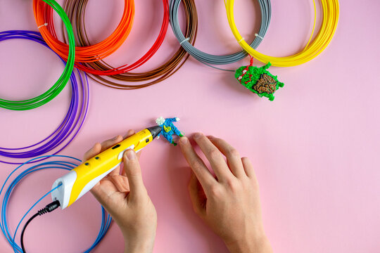 Children's hands create figures with a 3D pen on the pink background, top view