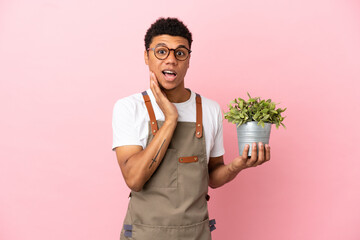 Gardener African man holding a plant isolated on pink background with surprise and shocked facial expression