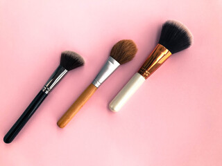 three tassels on a pink matte background. brushes for blush, powder, foundation and dry textures...