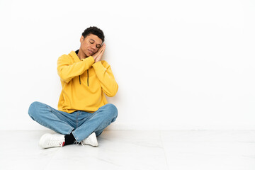 Young African American man sitting on the floor isolated on white background making sleep gesture in dorable expression