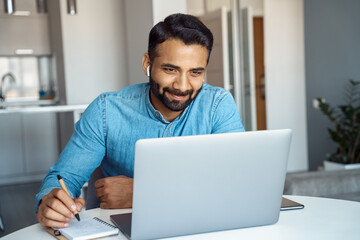 Portrait of mature adult indian man wearing earphones looking at laptop screen. Motivated student...