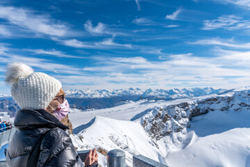 Fototapeta na wymiar Mature woman wearing face mask looking the snowy mountains and enjoying the day.