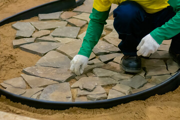 Builder worker hands in gloves laying garden paving slabs on sand - close up. Landscaping concept