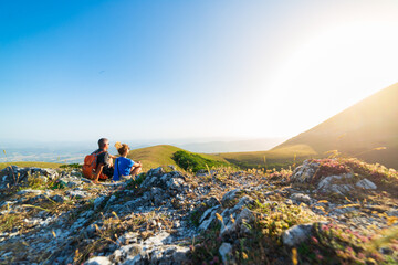 Man and woman hiking in the mountains of Umbria region, Monte Cucco, Appennino, Italy. Couple watching sunset together on mountain top. Summer outdoors activity.