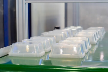 Stack of polypropylene food containers on conveyor belt of automatic plastic injection molding machine at exhibition, factory. Industry, manufacturing, automated technology concept