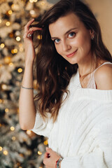 Beautiful lady in white sweater posing near decorated Christmas tree