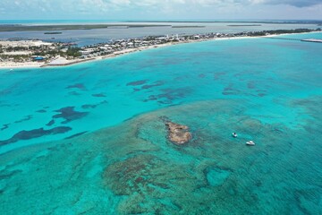 Aerial view of boats anchored near coral rocks with North Bimini coast in background on sunny summer afternoon.