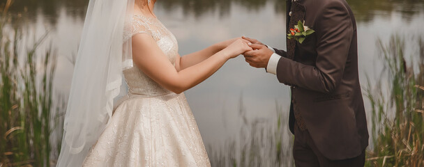 Fototapeta na wymiar Wedding. The bride in the wedding dress stands opposite the groom in a brown suit and holds hands outdoors