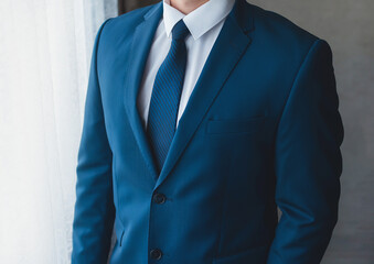 A businessman in a white shirt, a blue suit with a tie in front of the window, a close-up