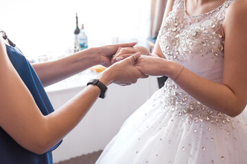 Obraz na płótnie Canvas Mom and bride in white dress hold hands, close-up