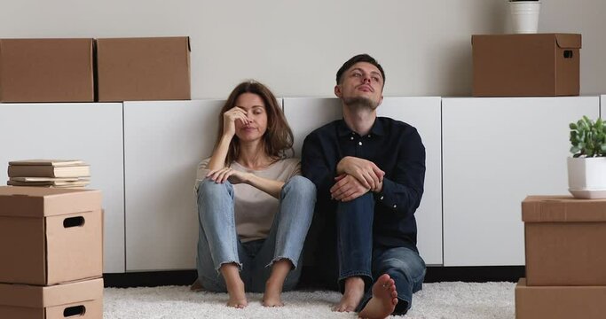 Near packed things, personal belongings in cardboard boxes tired young couple sit on floor, resting take break, reposing at moving day to new house. Long hard relocation, physical exhaustion concept