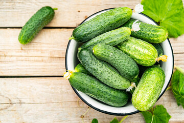 Bowl with fresh small crispy cucumbers over wooden background top view. Home growing concept. Copy space.