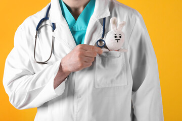 Pediatrician with toy bunny and stethoscope on yellow background, closeup