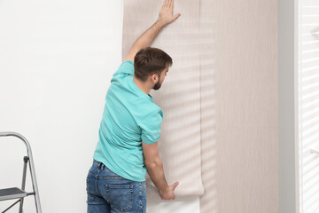 Fototapeta na wymiar Man hanging stylish wall paper sheet indoors