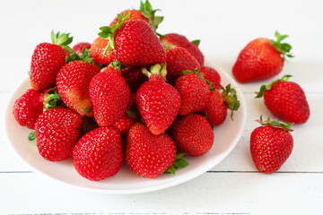 Plate of sweet red strawberries on white wooden table. Delicious summer berries.