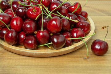 Red sweet cherry berries on a plate on wooden table, close up.