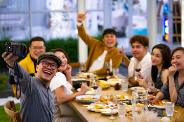 Group of Happy diversity Asian millennial people friends enjoy outdoor dinner party and using digital camera taking selfie together. Reunion friendship meeting celebration party and night life concept