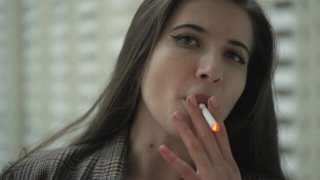 Attractive Caucasian Female Brunette wearing a Coat Smoking a Cigarette on the Balcony in Slow Motion