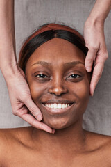 Vertical top down view at smiling African-American woman enjoying face massage and looking at camera