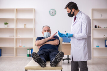 Fototapeta premium Old male patient visiting young male doctor in vaccination conce