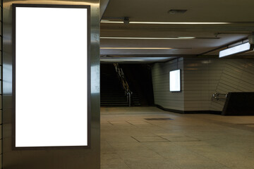 Vertical blank billboard on a glossy metal surface in a dark passageway underground.
