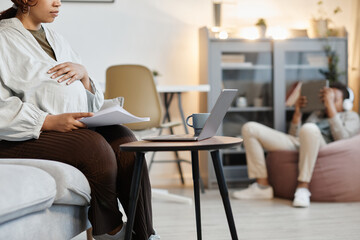 Cropped portrait of pregnant African-American woman using laptop at home with teenage son in background, copy space