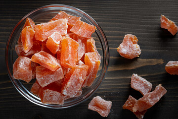 Natural farm homemade candied pumpkin fruits sprinkled with powdered sugar in a glass bowl on a wooden table, top view.