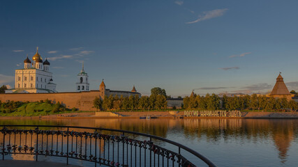 Fototapeta na wymiar View of the Pskov Kremlin at sunset. In the foreground is the border river Neman. On the embankment the text is laid out in large letters - Russia begins here