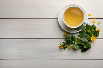 Fototapeta na wymiar Cup of aromatic celandine tea and flowers on white wooden table, flat lay. Space for text