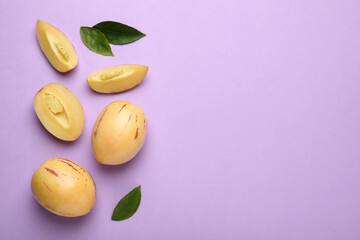 Whole and cut pepino melons with green leaves on violet background, flat lay. Space for text