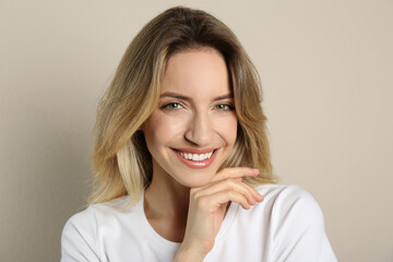 Portrait of happy young woman with beautiful blonde hair and charming smile on beige background