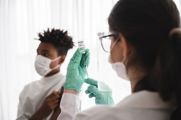 Female doctor or nurse wearing mask, gloves, and visor preparing to vaccinate coronavirus 19 to immunize African-American men.Concepts to prevent the spread of COVID-19.