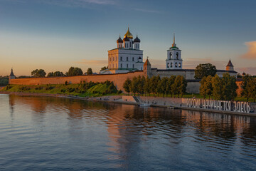 Fototapeta na wymiar View of the Pskov Kremlin at sunset. In the foreground is the border river Neman. On the embankment the text is laid out in large letters - Russia begins here